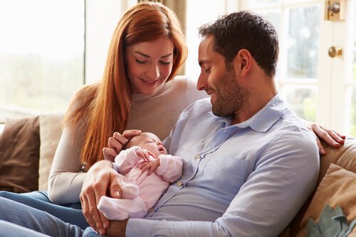 Mama i tata siedzący na kanapie, uśmiechający się do przytulanego noworodka