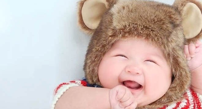 Roześmiane niemowlę w czapce z uszami misia - piąty miesiąc życia dziecka to zwiększone interakcje z otoczeniem