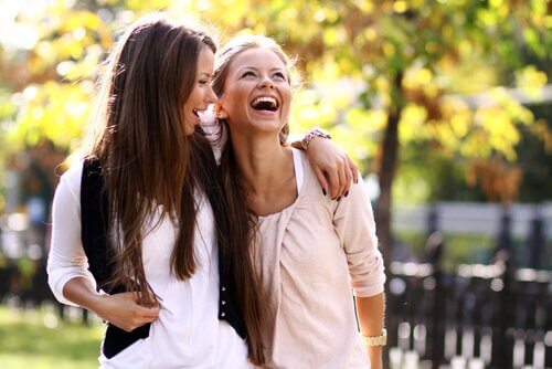 Roześmiane szatynka i blondynka idące razem przez park - by być lepszą mamą spędzaj czas z przyjaciółmi