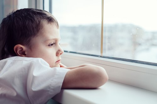 Smutny chłopiec wyglądający przez okno z rękoma opartymi na parapecie