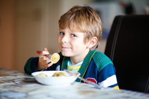 Uśmiechnięty chłopiec siedzący przy stole i jedzący z miski - zespół przeżuwania