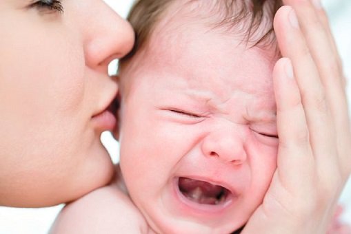 Mama całująca w główkę płaczące niemowlę