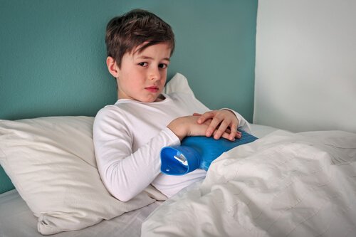 Smutny chłopiec leżący w łóżku z termoforem na brzuchu