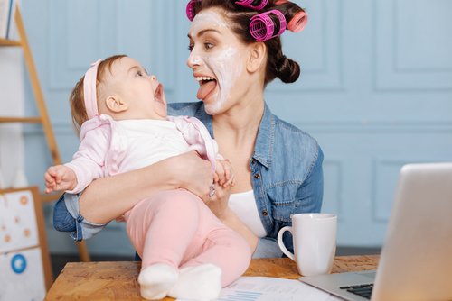 Zapewnić rozrywkę dziecku - mama w maseczce na twarzy rozśmiesza niemowlę