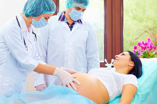 Kobieta w ciąży leżąca na leżance i dwóch lekarzy badających jej brzuch