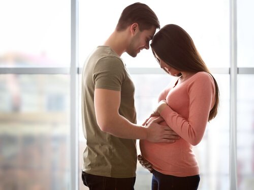 Uśmiechnięty mężczyzna trzymający dłonie na brzuchu kobiety w ciąży