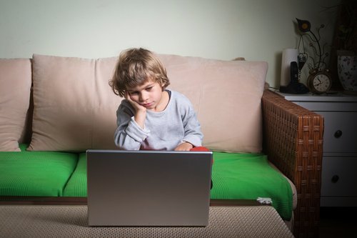 Znudzony chłopiec siedzący na kanapie wpatrzony w laptopa - lenistwo u dzieci