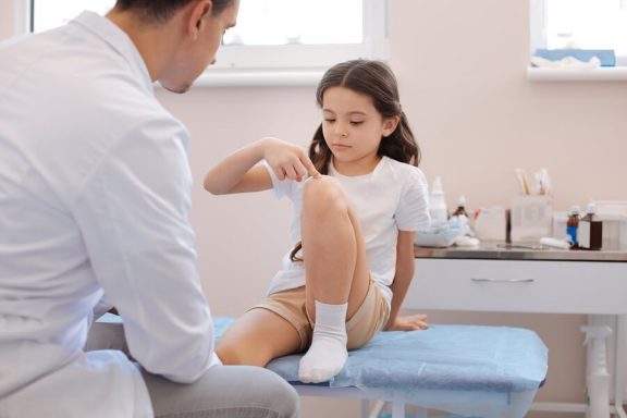 Dziewczynka pokazuje na kolano podczas wizyty u lekarza