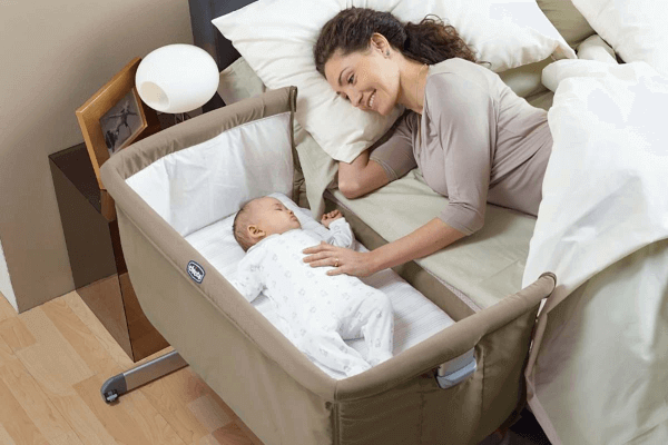 Mama leżąca na łóżku głaszcząca dziecko w przystawionym łóżeczku