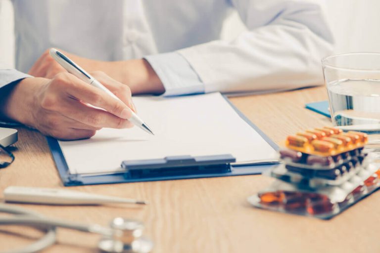 Lekarz piszący na kartce, na pierwszym planie leki