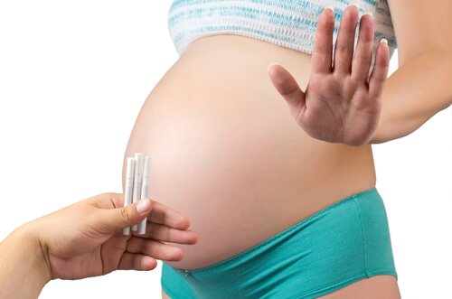 Papierosy na tle brzucha w ciąży i kobieta odmawiająca ich przyjęcia gestem dłoni