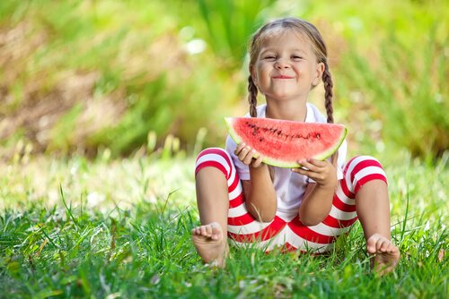 Uśmiechnięta dziewczynka siedząca na łące i jedząca arbiza