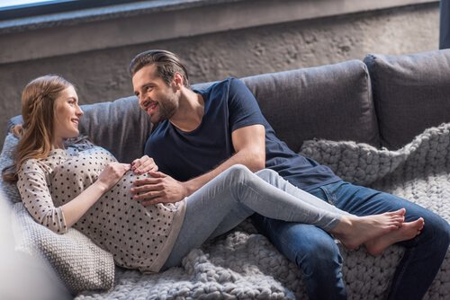 Uśmiechnięta kobieta w ciąży i mężczyzna leżący przytuleni na kanapie - instrukcja dla świeżo upieczonych rodziców