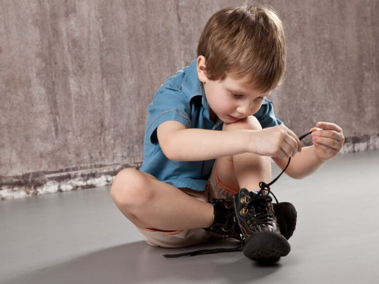 Chłopiec siedzący na podłodze i wiążący buty