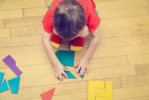 Chłopiec układający na podłodze figury z pociętych kolorowych kartek - ćwiczenia na koncentrację dla dzieci 