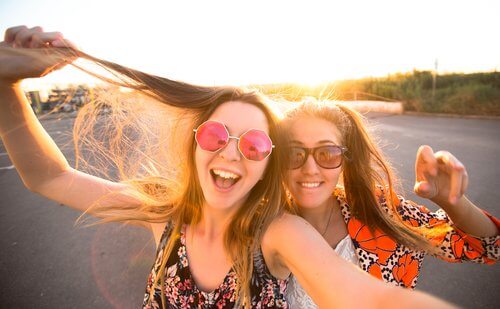 Dwie uśmiechnięte nastolatki w okularach przeciwsłonecznych robiące sobie selfie