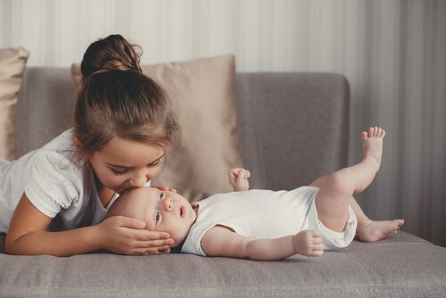 Dziewczynka całująca niemowlę leżące na kanapie w główkę