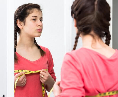 Dziewczynka w lustrze mierząca obwód biustu - rozwój i dorastanie dziewczynek