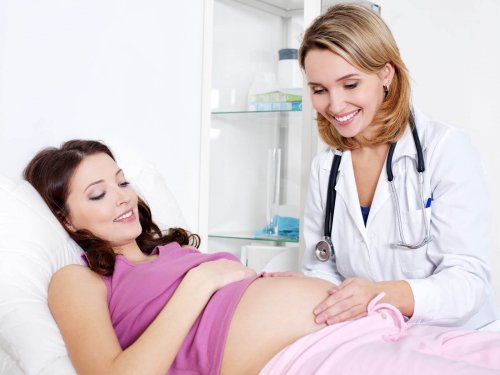 Ginekolog badająca brzuch leżącej ciężarnej kobiety - badania w ciąży