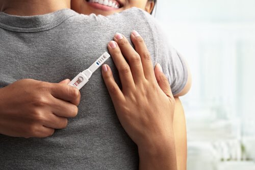 Kobieta trzymająca w dłoni test ciążowy i przytulająca mężczyznę - najlepsza pora roku na zajście w ciążę