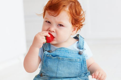 Rude dziecko w ogrodniczkach jedzące truskawkę