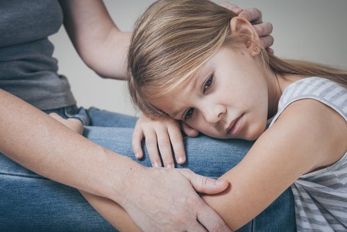Smutna dziewczynka kładąca głowę na kolanach mężczyzny - nieobecność ojca i jej konsekwencje