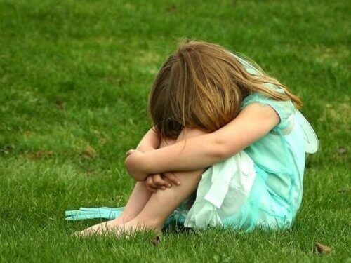 Smutne dziecko siedzi skulone na trawie