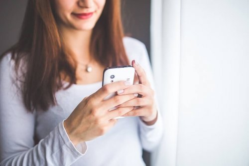Uśmiechnięta kobieta wpatrzona w ekran telefonu
