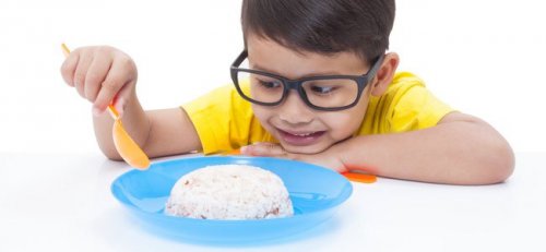Uśmiechnięty chłopiec w okularach jedzący łyżką ryż