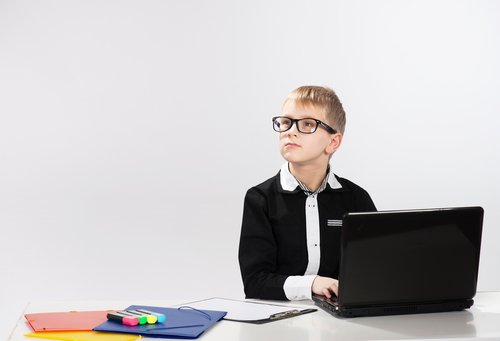 Chłopiec w garniturze i okularach przy laptopie