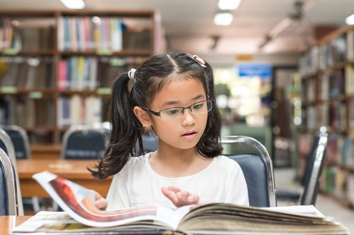 Dziewczynka w okularach czytająca w bibliotece - jak wspierać utalentowane dziecko