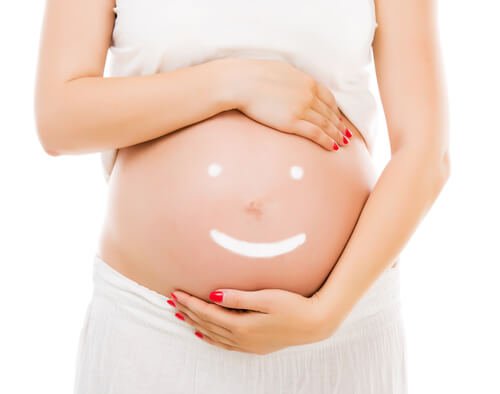 Kobieta obejmująca brzuch w ciąży z narysowaną, uśmiechniętą buzią
