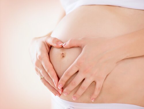 Mama obejmująca brzuch i robiąca serce z palców