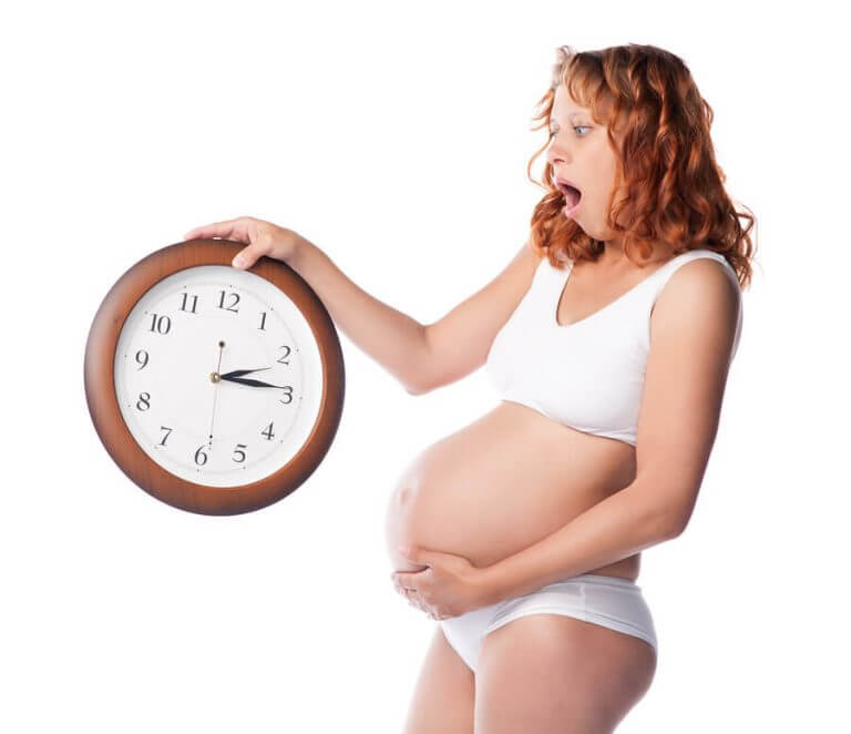 Przestraszona kobieta w ciąży trzymająca zegar - jak pokonać strach przed porodem