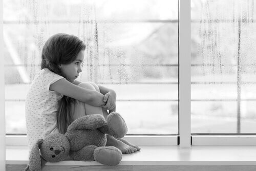 Smutna dziewczynka siedząca skulona na parapecie