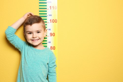 Uśmiechnięty chłopiec stojący przy miarce na ścianie - rozwój chłopca