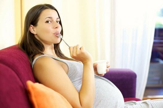 Kobieta w ciąży na kanapie jedząca jogurt