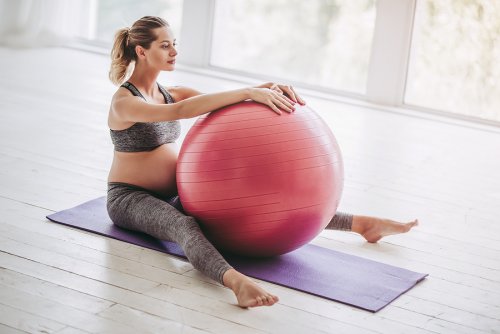 Kobieta w ciąży siedząca na macie z piłką do ćwiczeń