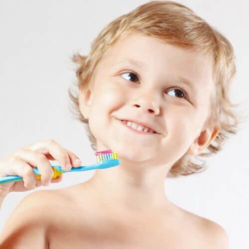 Uśmiechnięty chłopiec trzymający szczoteczkę do zębów - jak wyrobić dobre nawyki w dziecku