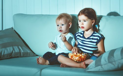 Dziewczynka i chłopiec oglądający telewizję i jedzący popcorn