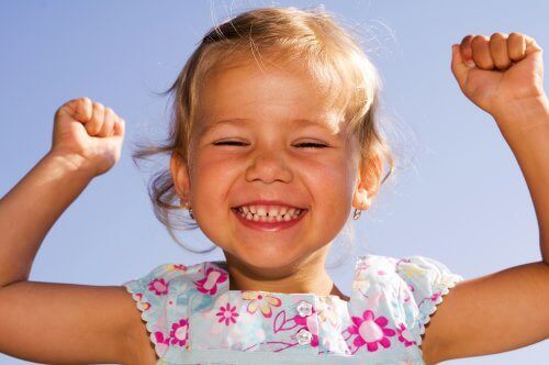 Szczęśliwa dziewczynka unosząca ręce do góry - jak obudzić w dziecku optymizm?