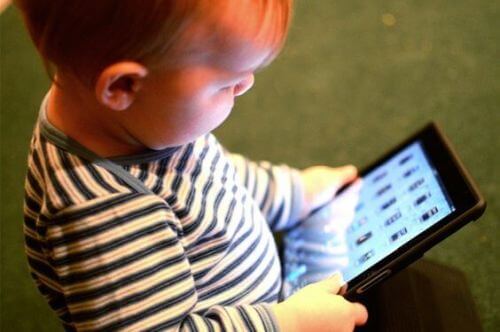 Dziecko siedzi z tabletem, który czasami może opóźniać rozwój mowy