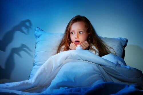 Przerażona dziewczynka w łóżku bojąca się ciemności - lęki u dzieci