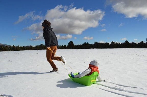 Tata ciągnący dziecko na sankach - zabawy w śniegu